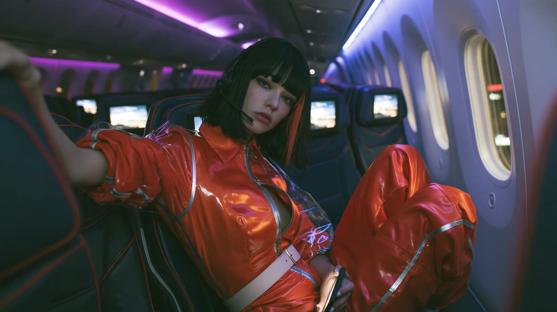 Jet-set high fashion editorial, a couture magazine story shot on a night flight: a medium-wide shot from the aisle of a Caucasian American woman in her late twenties with pale skin and a glossy black blunt bob with…