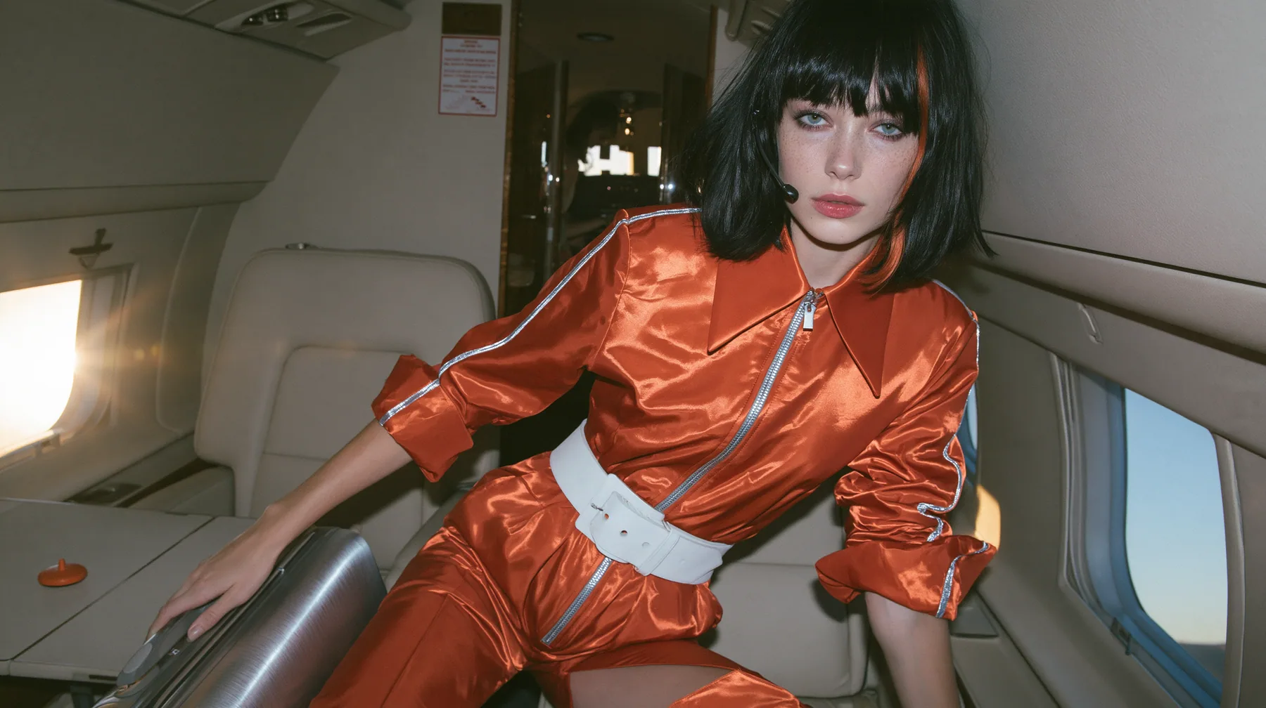 Jet-set high fashion editorial, a couture magazine story shot on a morning arrival: a medium-wide shot of a Caucasian American woman in her late twenties with pale skin and a glossy black blunt bob with heavy…