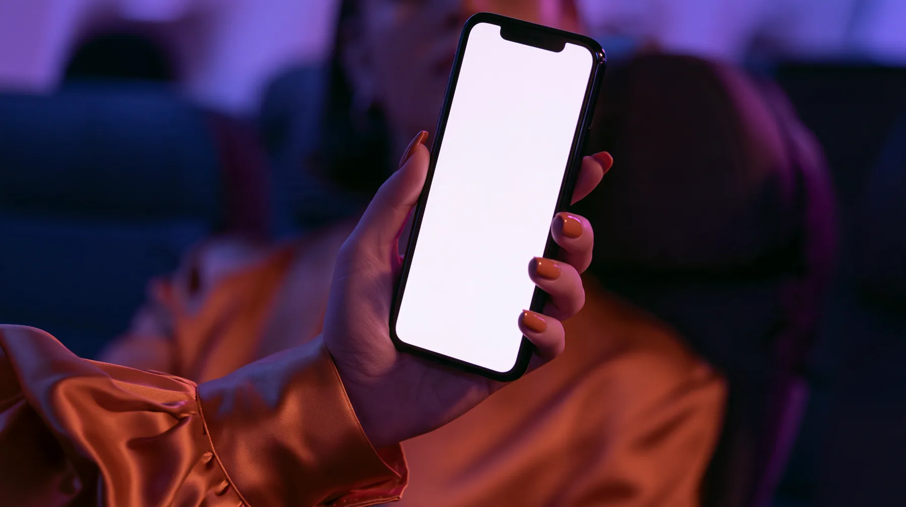 Jet-set editorial still life: an extreme close-up of a woman's hand with clay-orange nail polish holding a glossy black smartphone upright toward the lens, its screen a blank glowing white, the sleeve of a glossy…