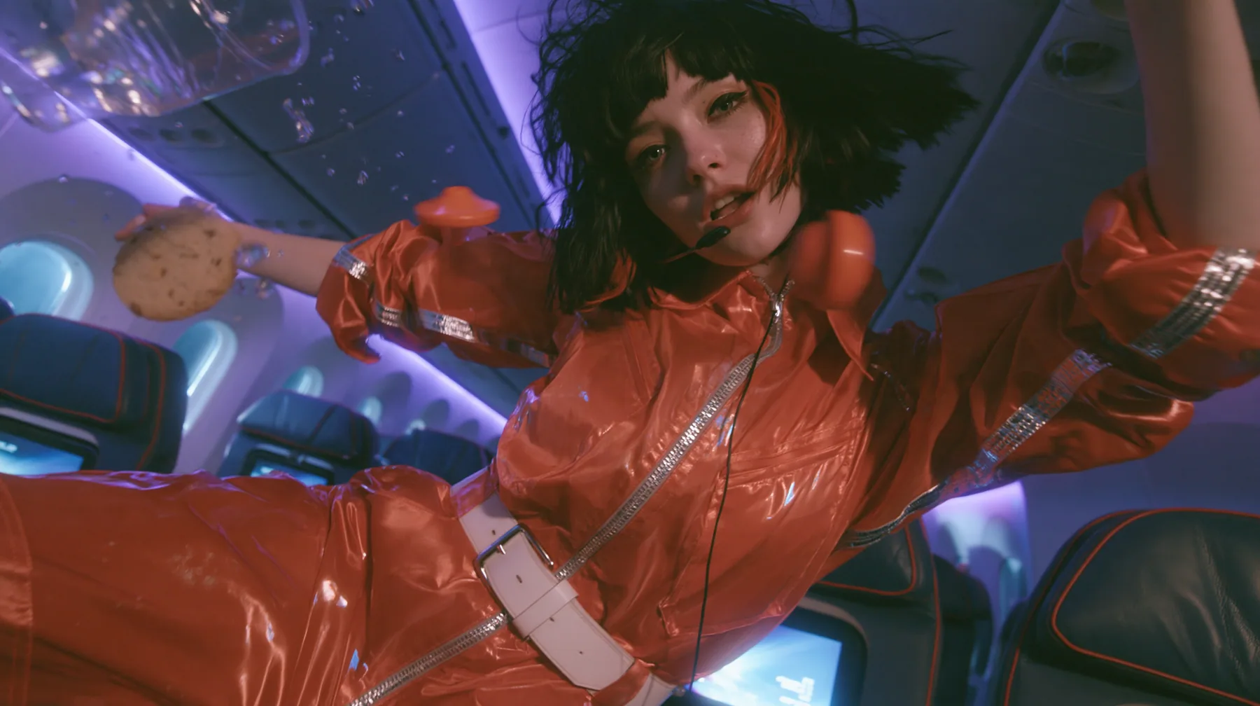 Jet-set high fashion editorial, a couture magazine story shot on a night flight: a medium-wide shot of a Caucasian American woman in her late twenties with pale skin and a glossy black blunt bob with heavy straight…