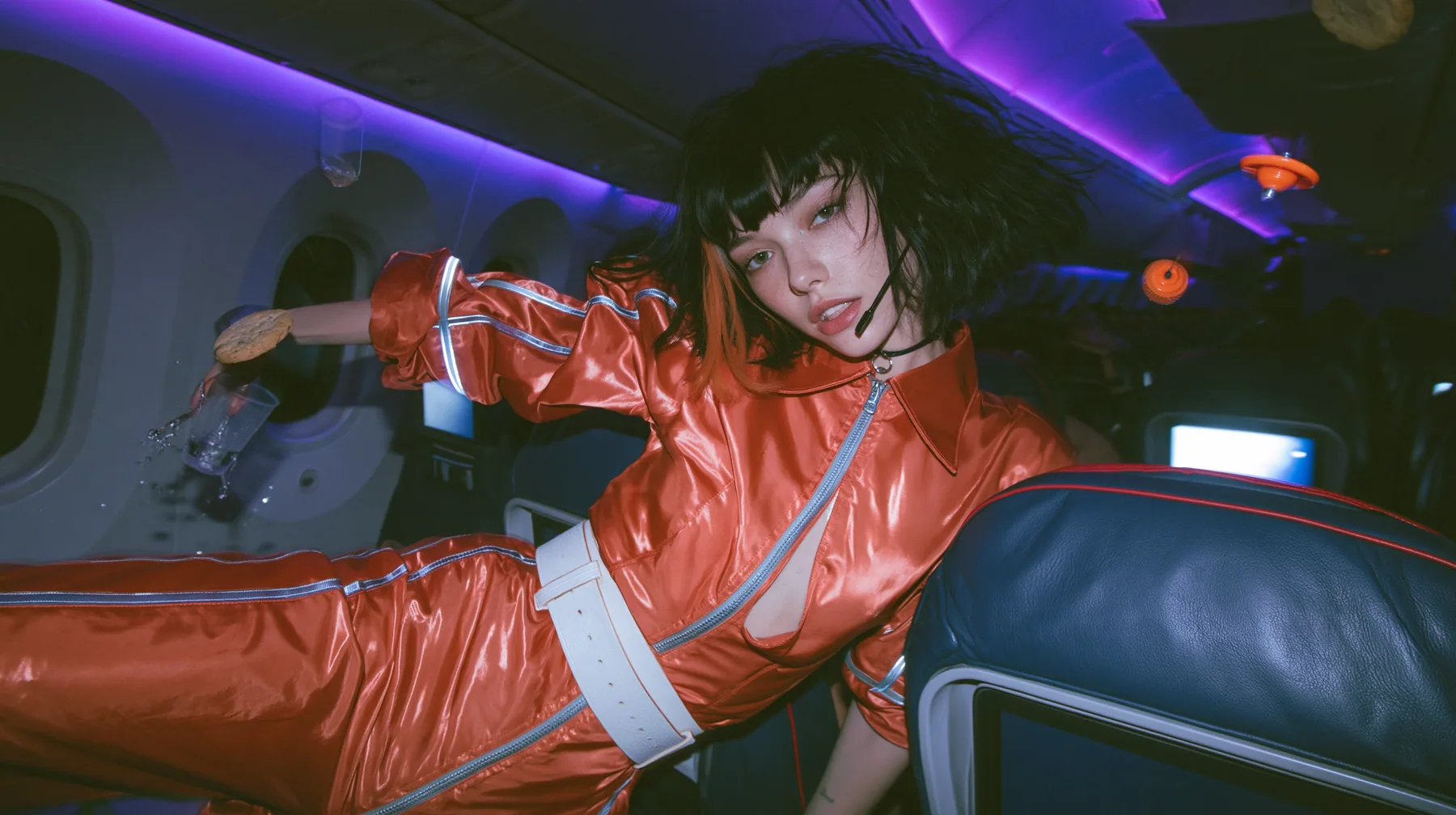Jet-set high fashion editorial, a couture magazine story shot on a night flight: a medium-wide shot of a Caucasian American woman in her late twenties with pale skin and a glossy black blunt bob with heavy straight…