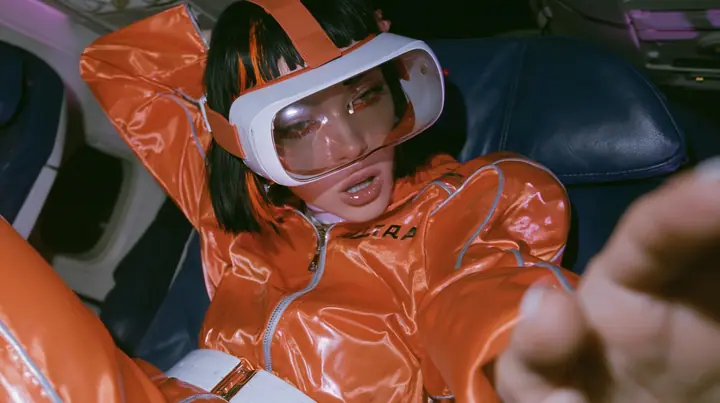 Jet-set fashion editorial, night flight: medium close-up of a woman in a glossy international-orange satin flight jumpsuit with silver piping and a white belt with a black bob and one orange streak, a glossy white VR…