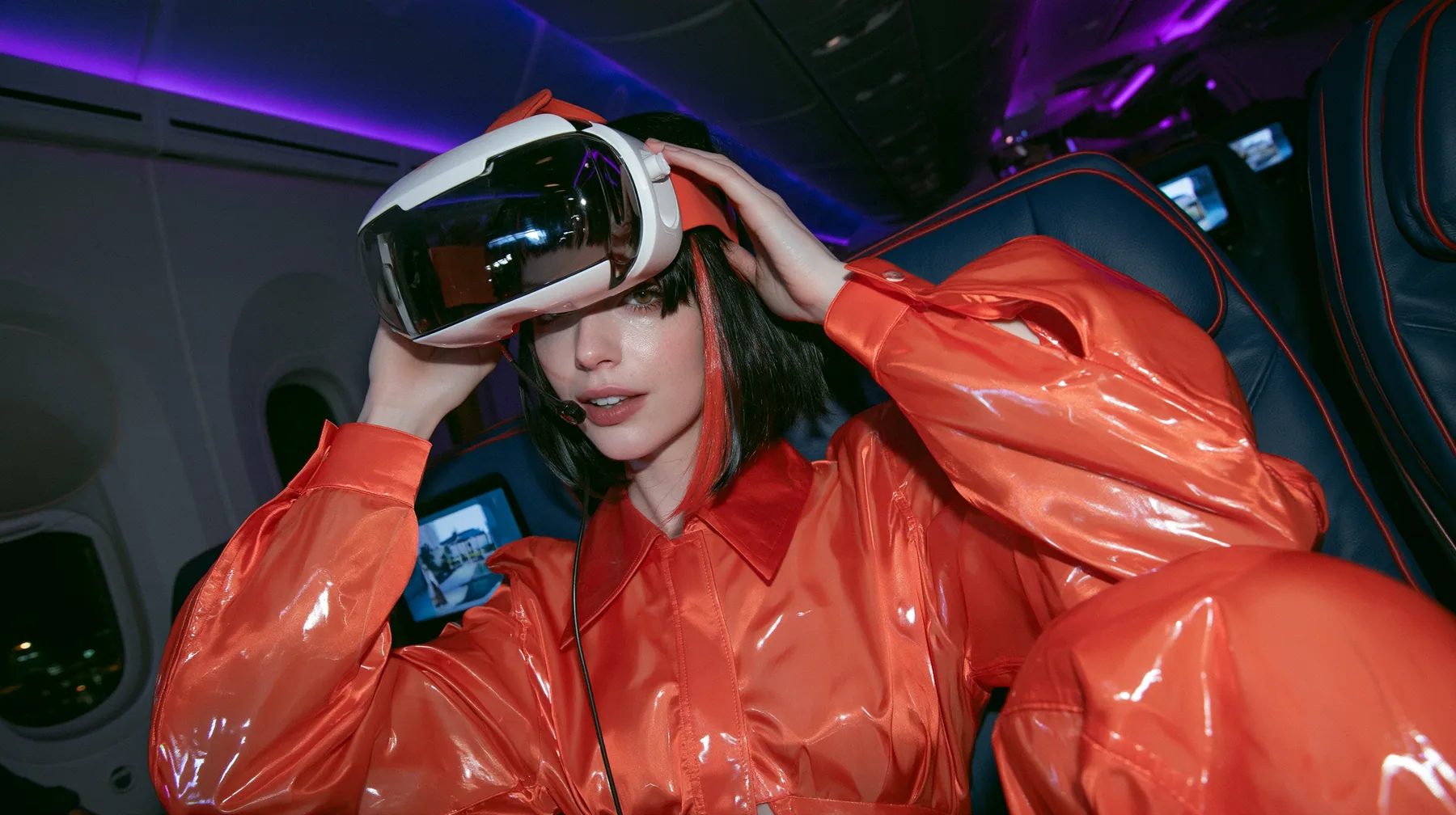 Jet-set fashion editorial, night flight: a medium close-up of a Caucasian American woman in her late twenties with pale skin and a glossy black blunt bob with heavy straight bangs and one clay-orange streak, a thin…
