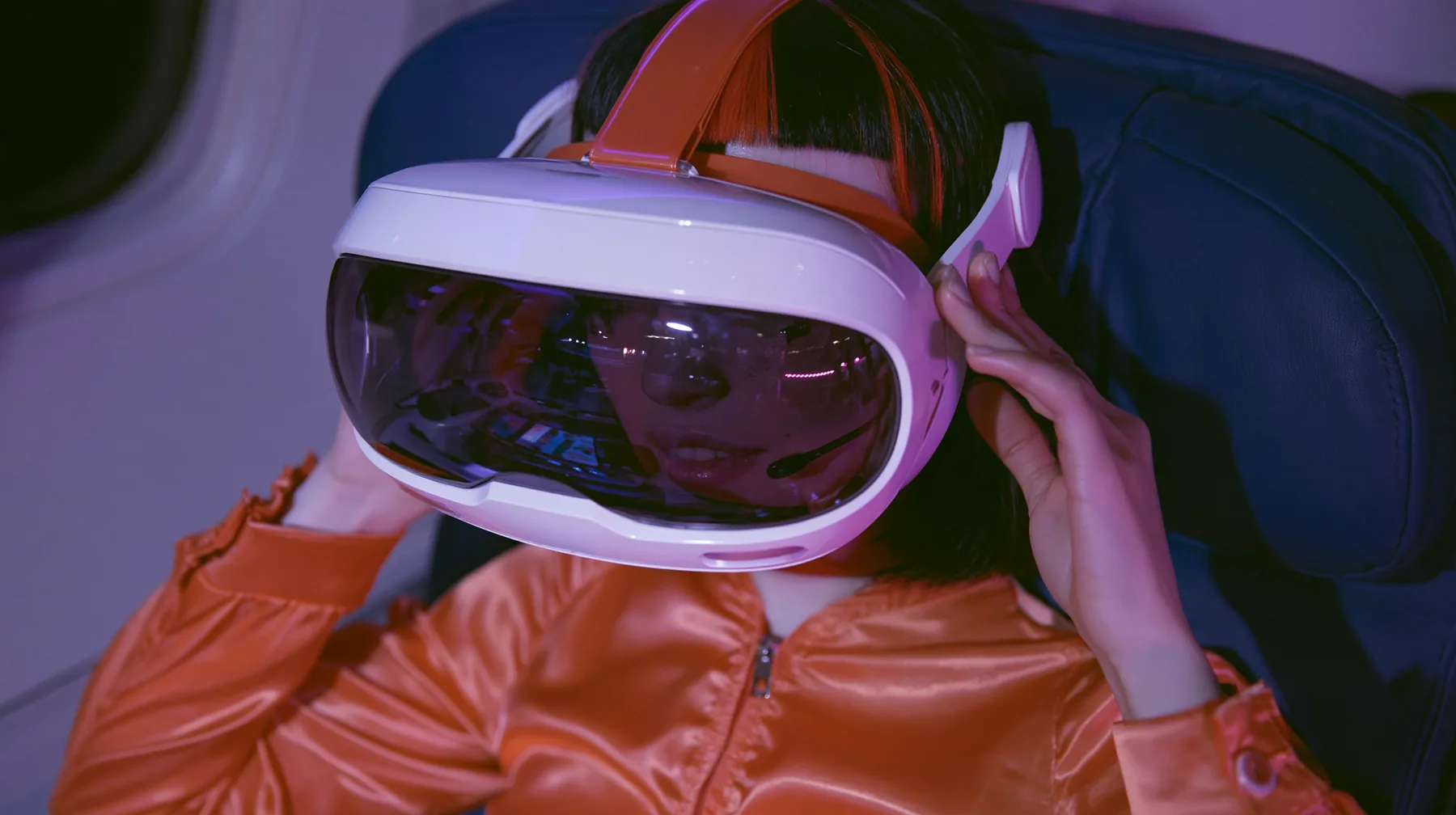 Jet-set fashion editorial, night flight: a medium close-up of a Caucasian American woman in her late twenties with pale skin and a glossy black blunt bob with heavy straight bangs and one clay-orange streak, a thin…