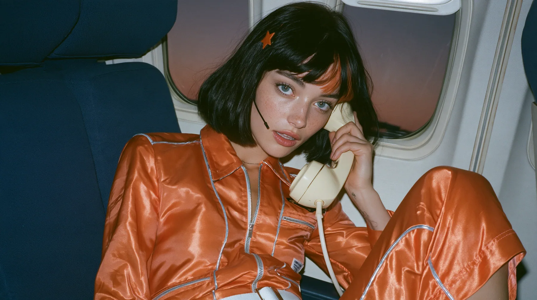 Jet-set fashion editorial, dusk flight: an eye-level medium shot of a Caucasian American woman in her early thirties, a grown woman with elegant mature features, an angular face and defined cheekbones, pale freckled…