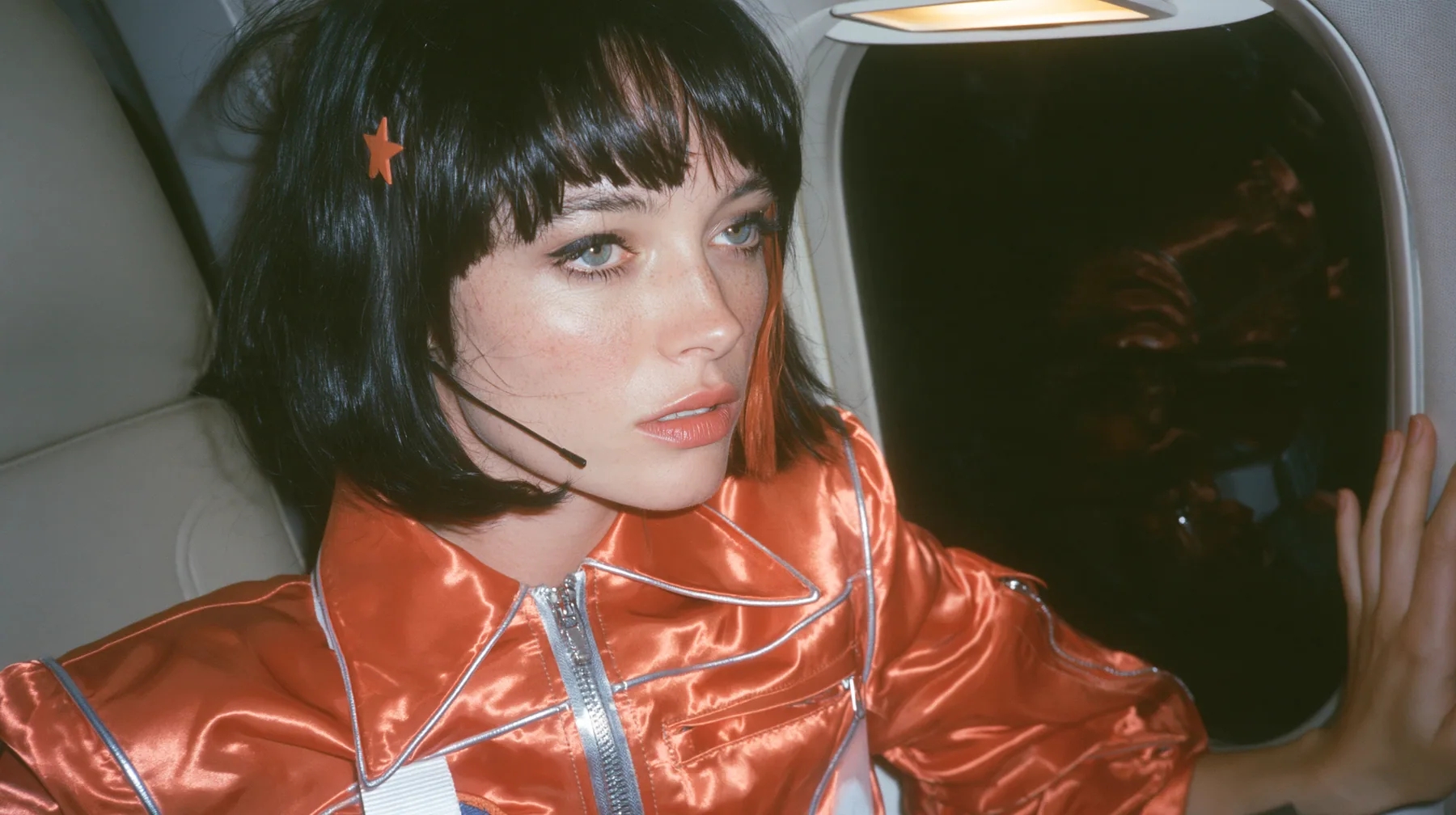 Jet-set fashion editorial, night flight: an eye-level close profile of a Caucasian American woman in her early thirties, a grown woman with elegant mature features, an angular face and defined cheekbones, pale…
