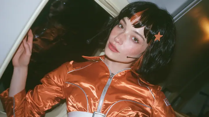 Jet-set fashion editorial, night flight: an eye-level close three-quarter profile of a Caucasian American woman in her early thirties, a grown woman with elegant mature features, an angular face and defined…