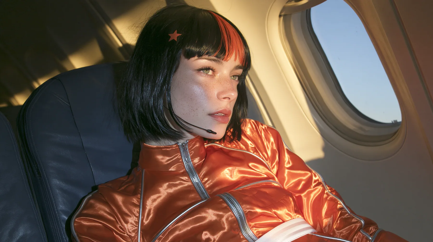 Jet-set fashion editorial, dawn flight: an eye-level medium close-up of a Caucasian American woman in her early thirties, a grown woman with elegant mature features, an angular face and defined cheekbones, pale…
