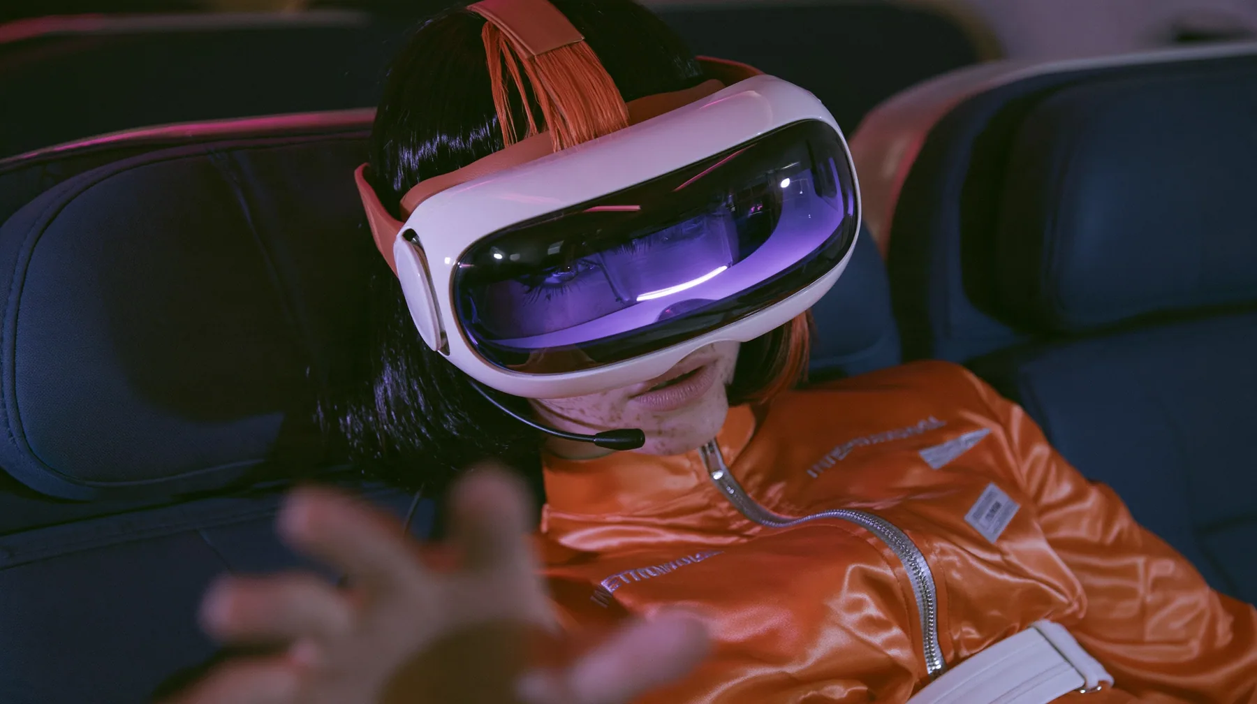 Jet-set fashion editorial, night flight: a Caucasian American woman in her early thirties, an angular adult face, pale freckled skin, a glossy black blunt bob with heavy bangs and one clay-orange streak, a thin black…