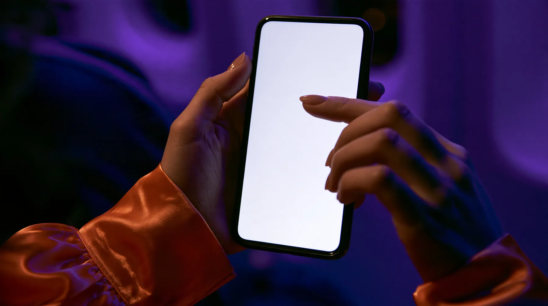 Editorial macro, night flight: a pale woman's left hand with short natural nails holds a black smartphone upright, its blank bright white screen toward the camera, the index finger of her right hand touching the…