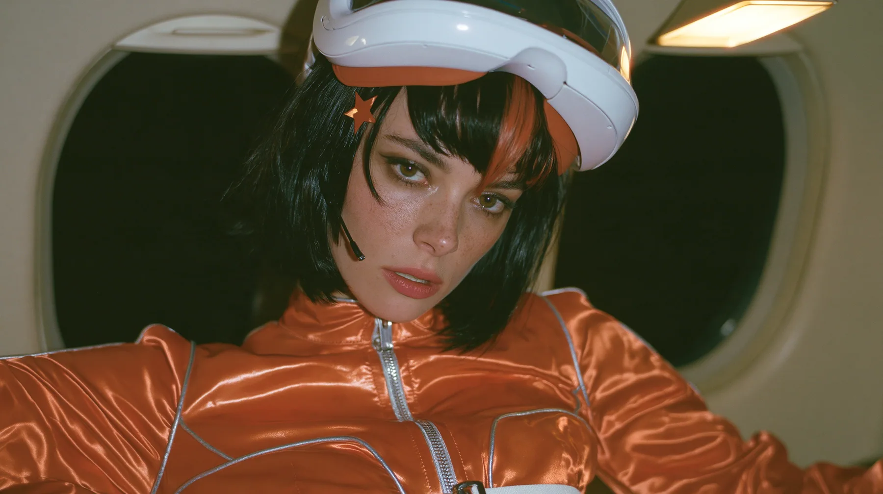 Jet-set fashion editorial, night flight: a close-up portrait of a Caucasian American woman in her early thirties, a grown woman with elegant mature features, an angular face and defined cheekbones, pale freckled…