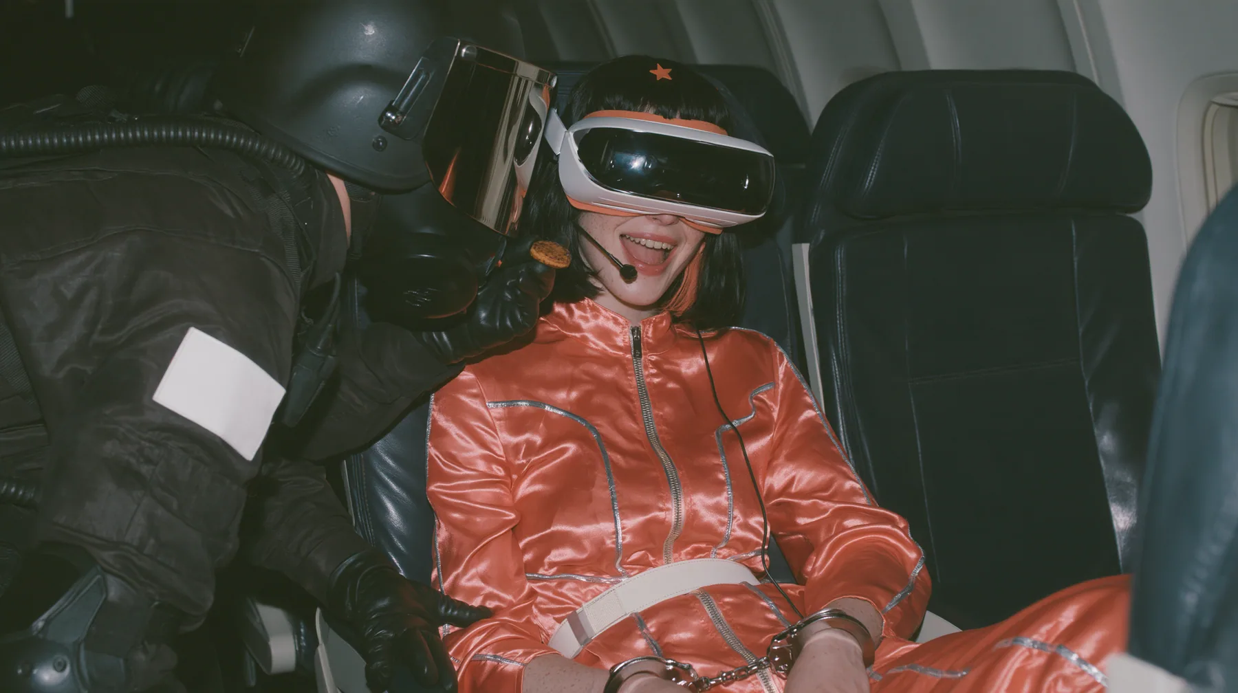 Cinematic film still, night airliner cabin with navy leather seats, all of them empty: a Caucasian woman in her early thirties with an angular adult face, pale freckled skin, a glossy black blunt bob with heavy bangs…