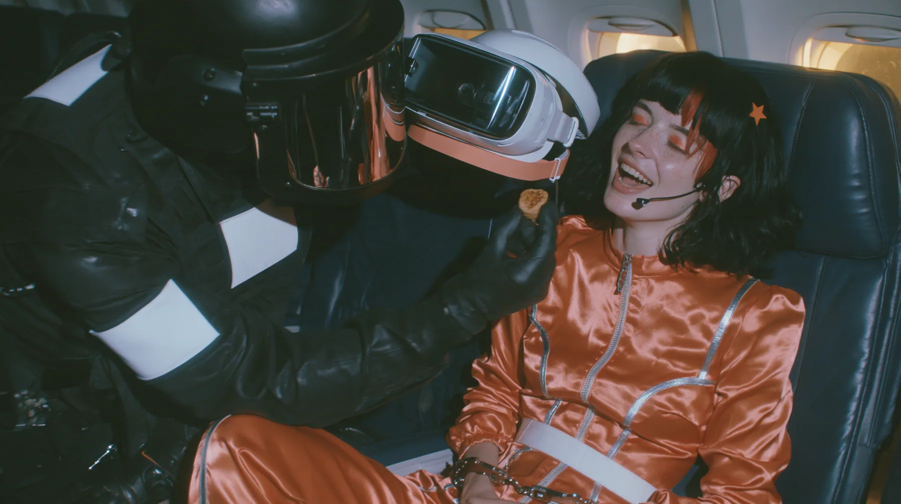 Cinematic film still, night airliner cabin with navy leather seats, all of them empty: a Caucasian woman in her early thirties with an angular adult face, pale freckled skin, a glossy black blunt bob with heavy bangs…