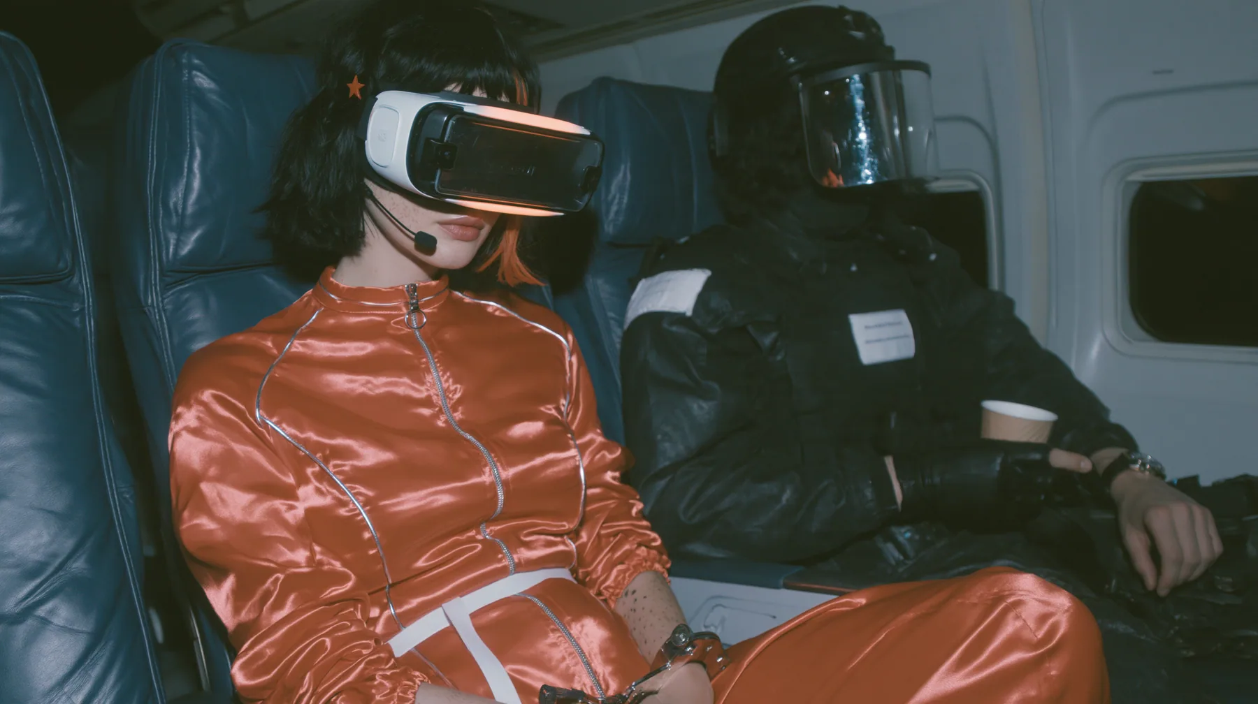 Cinematic film still at 3 AM, dim blue night airliner cabin with navy leather seats, all of them empty: a Caucasian woman in her early thirties with an angular adult face, pale freckled skin, a glossy black blunt bob…