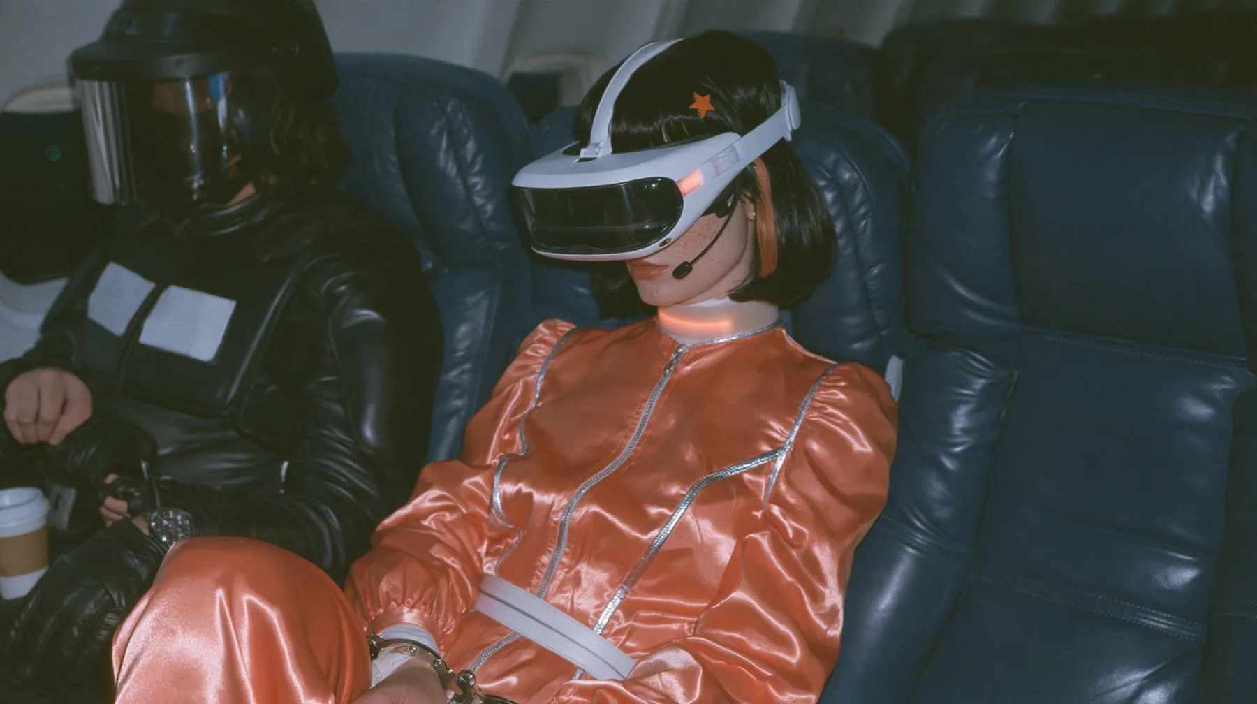 Cinematic film still at 3 AM, dim blue night airliner cabin with navy leather seats, all of them empty: a Caucasian woman in her early thirties with an angular adult face, pale freckled skin, a glossy black blunt bob…