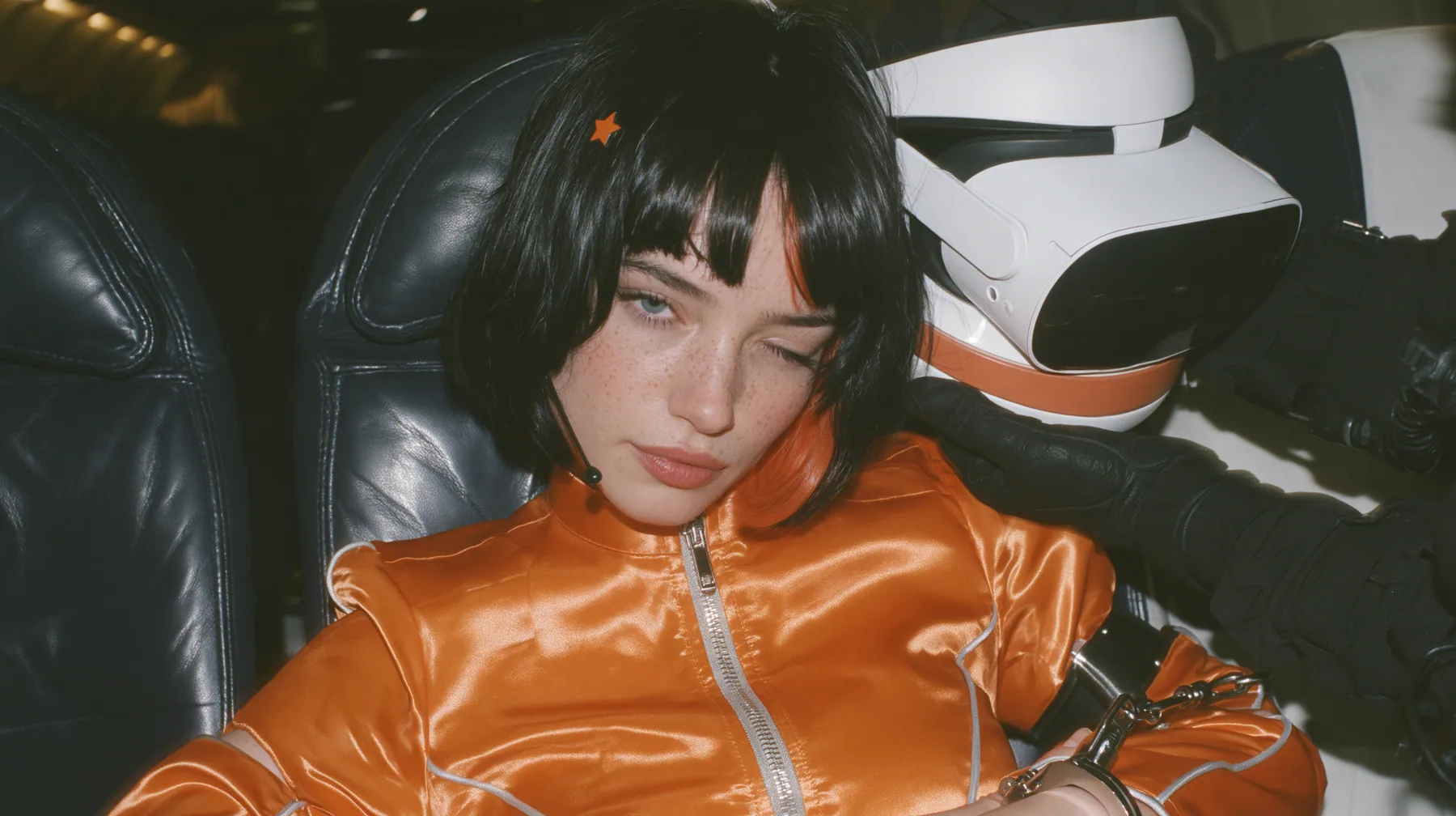 Close-up film still at eye level: a 32-year-old grown woman with elegant mature features, defined cheekbones and an angular jaw, pale freckled skin, a glossy black blunt bob with heavy bangs and one clay-orange…