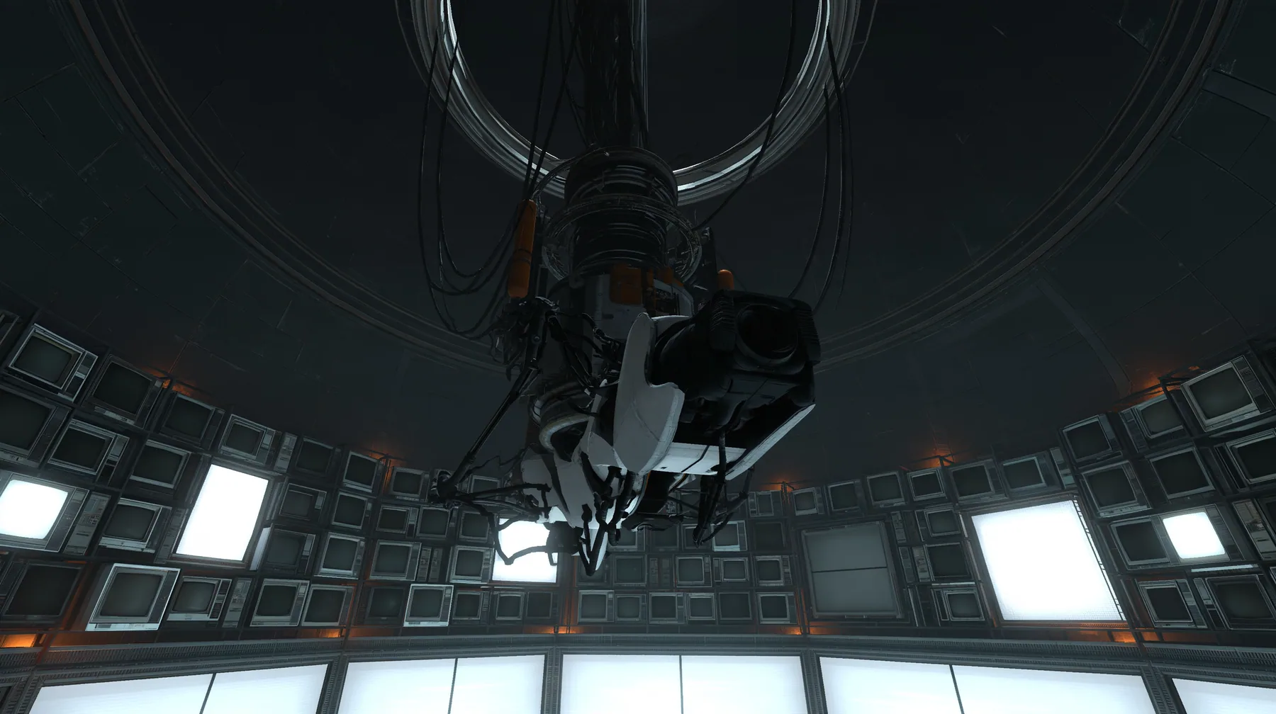 the same dark circular AI chamber with the ceiling ring and hanging cables, its curved walls now lined floor to ceiling with dozens of old CRT monitors and flat panel screens glowing faint white, warm amber accent…