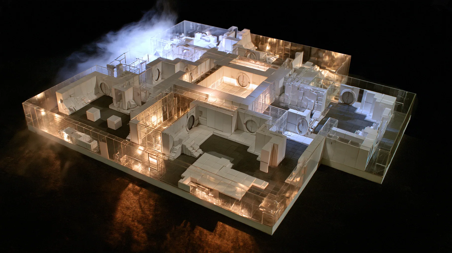 Valve's Portal 2 as a neural network dreams it, a Source engine render: top-down view of a miniature white Aperture Science training chamber at dollhouse scale on a dark floor: tiny white panels, tiny round doors,…
