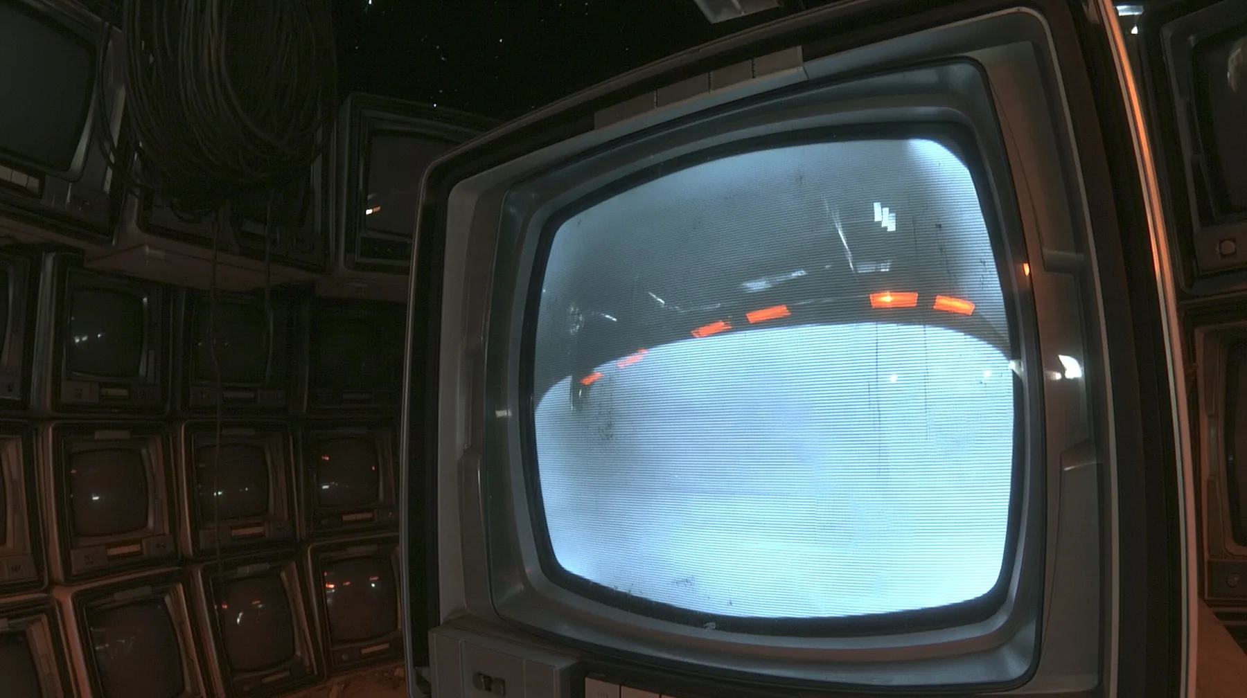 extreme macro shot of the curved glass of a single 1970s CRT monitor waking up in a pitch-dark machine chamber, a faint green-white phosphor bloom swelling at the centre of the screen, one blinking block cursor, fine…