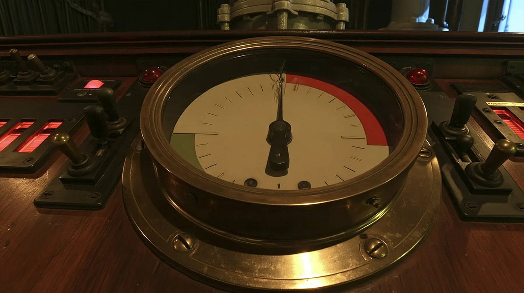 macro close-up of a big brass-bezelled analog gauge on a wooden 1960s control console: a cream dial face with a red zone at the upper right and a green zone at the left, plain tick marks, the black needle trembling…
