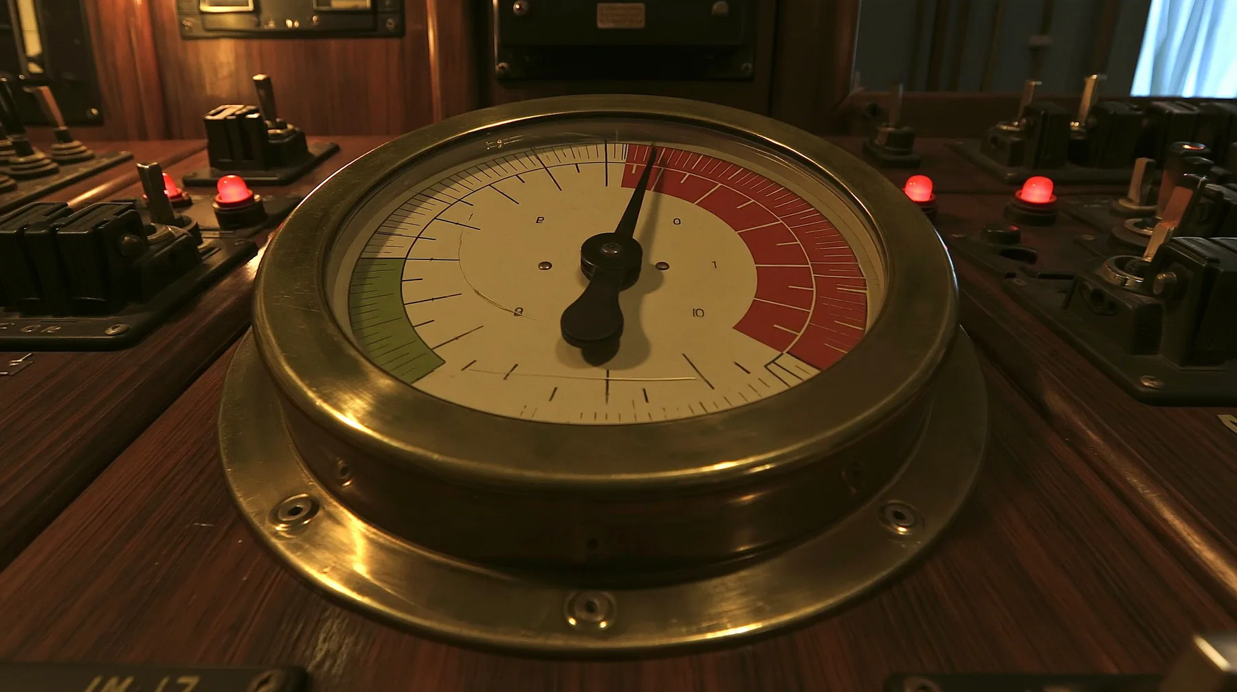 macro close-up of a big brass-bezelled analog gauge on a wooden 1960s control console: a cream dial face with a red zone at the upper right and a green zone at the left, plain tick marks, the black needle trembling…