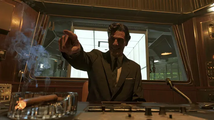 low-angle cinematic shot in a 1950s observation booth: a lean grinning executive with a long face, a long straight nose, a big toothy showman's grin, a dark wavy pompadour, a charcoal suit and thin dark tie points…