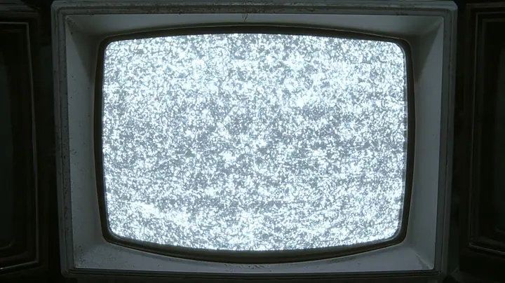 cinematic straight-on close-up of a battered 1970s CRT monitor whose rounded screen fills almost the whole frame, boiling with bright white television static, a scuffed grey-white plastic bezel around it, slivers of…