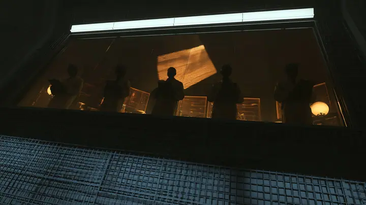 Low-angle cinematic film still: a long tilted observation window set high in a dark lattice wall, five silhouetted scientists in lab coats lined up behind the glass with clipboards, glowing amber monitors and round…