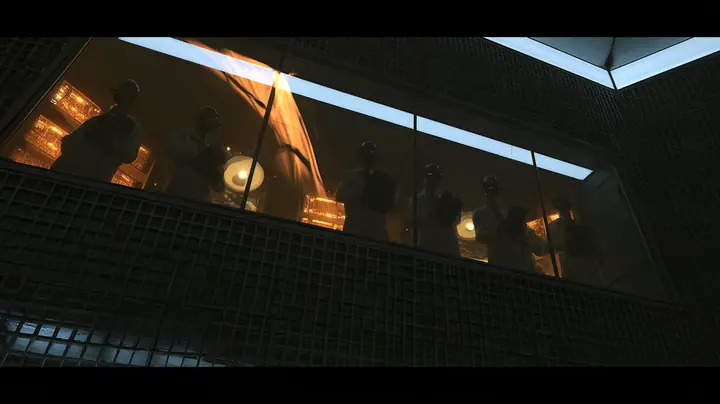 Low-angle cinematic film still: a long tilted observation window set high in a dark lattice wall, five silhouetted scientists in lab coats lined up behind the glass with clipboards, glowing amber monitors and round…