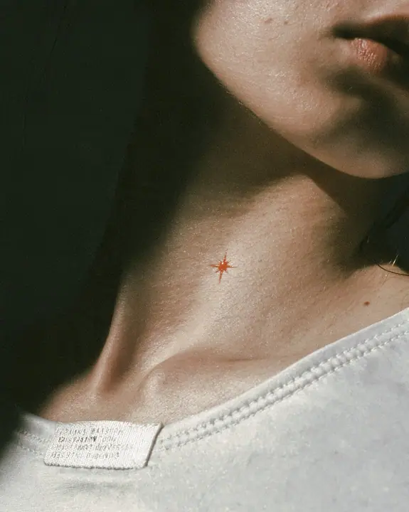 macro fashion-editorial close-up of a young woman's collarbone and jaw, a stitched technical woven label with tiny serial codes and a clay-orange eight-pointed spark on matte white ripstop, razor-thin focus, soft…