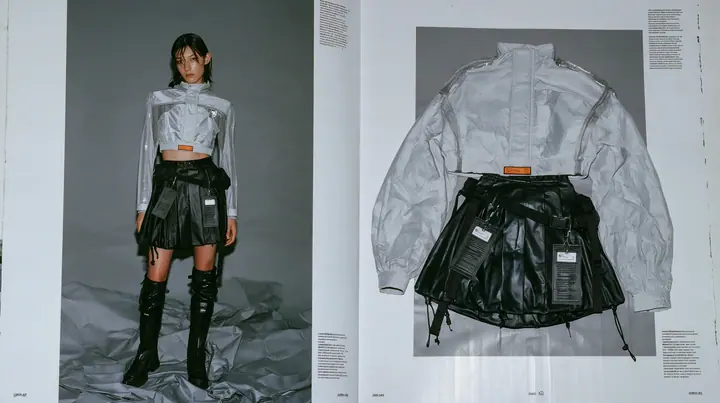 two-page techwear lookbook spread: on the left a full-length photograph of a young woman in a technical cropped shell top in pale grey ripstop with taped seams and a woven label at the hem, high-waisted pleated…