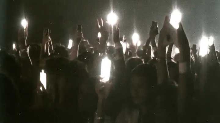 a 1-bit ordered-dither photocopy of a crowd of silhouetted fashion-show guests holding up glowing phones, coarse dither in black toner on off-white paper, copier edge burn, one scanline drop-out band, no grey tones,…