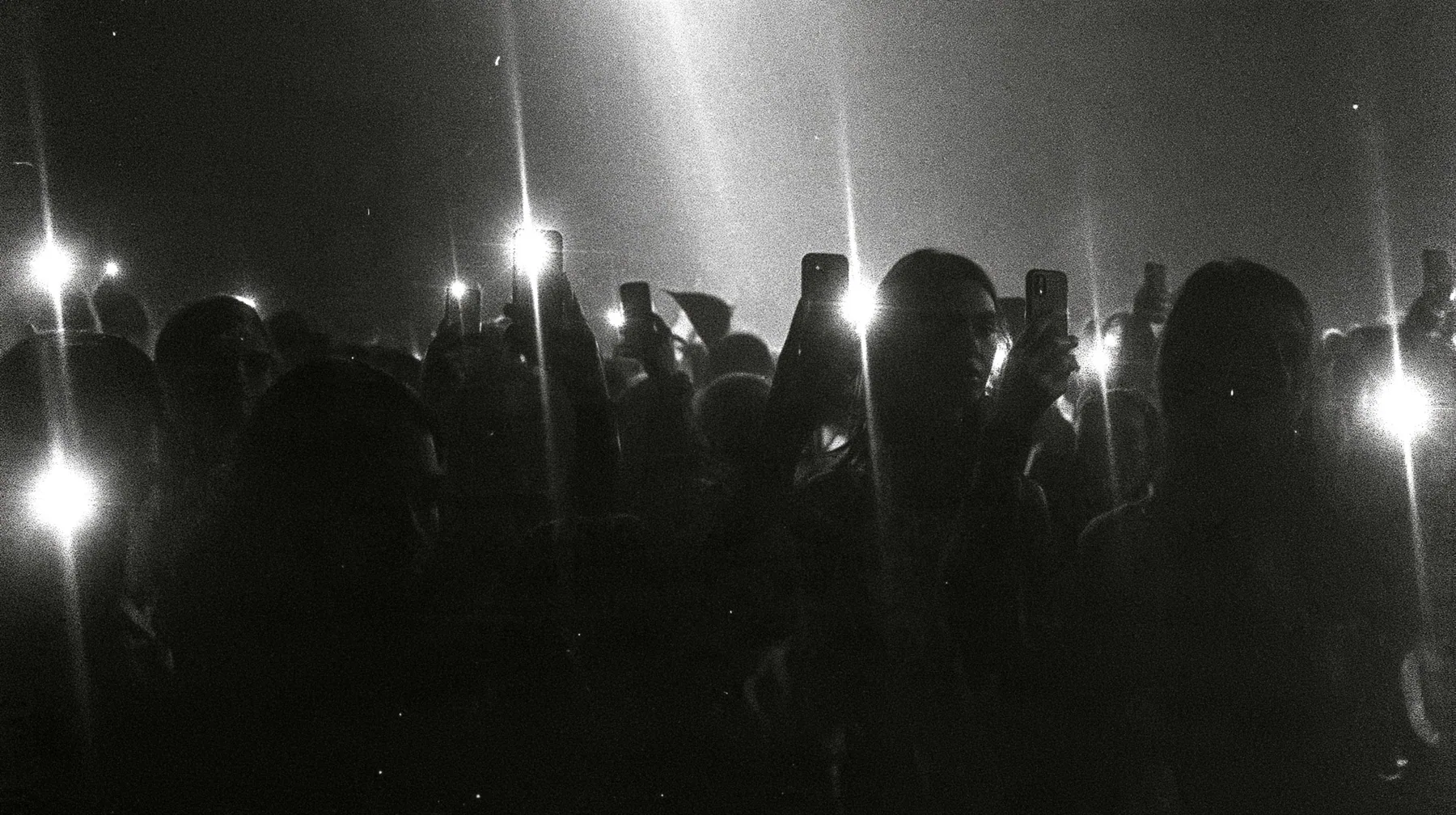 a 1-bit ordered-dither photocopy of a crowd of silhouetted fashion-show guests holding up glowing phones, coarse dither in black toner on off-white paper, copier edge burn, one scanline drop-out band, no grey tones,…