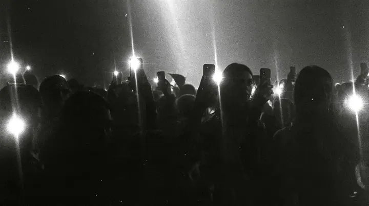 a 1-bit ordered-dither photocopy of a crowd of silhouetted fashion-show guests holding up glowing phones, coarse dither in black toner on off-white paper, copier edge burn, one scanline drop-out band, no grey tones,…