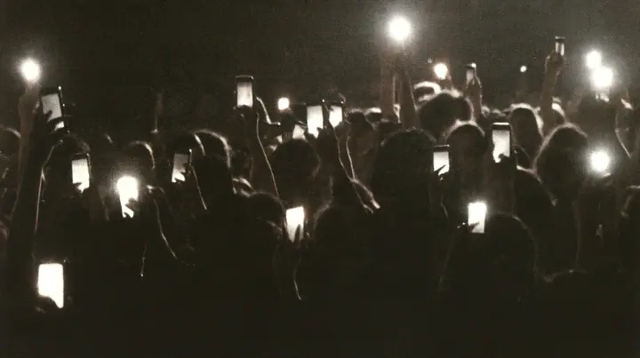 a 1-bit ordered-dither photocopy of a crowd of silhouetted fashion-show guests holding up glowing phones, coarse dither in black toner on off-white paper, copier edge burn, one scanline drop-out band, no grey tones,…