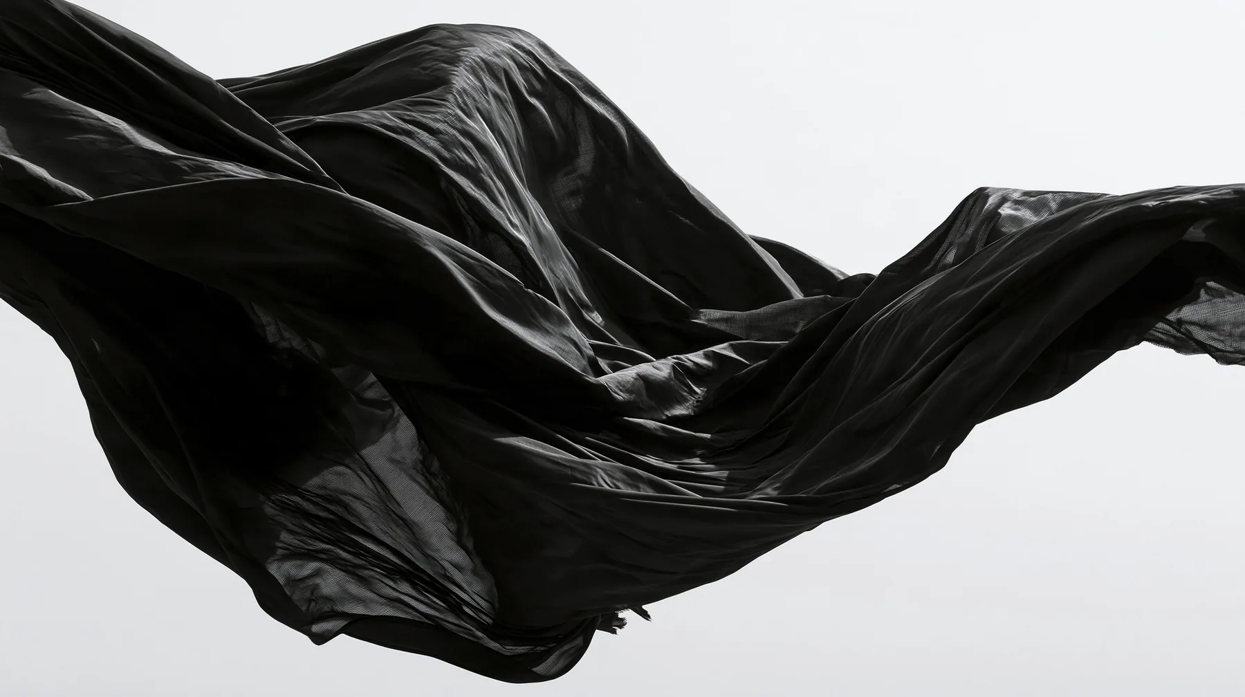 black technical nylon fabric rippling violently in wind against white, dramatic folds, high-contrast monochrome studio photograph, fine grain, no text, no letters, no logos, no watermark