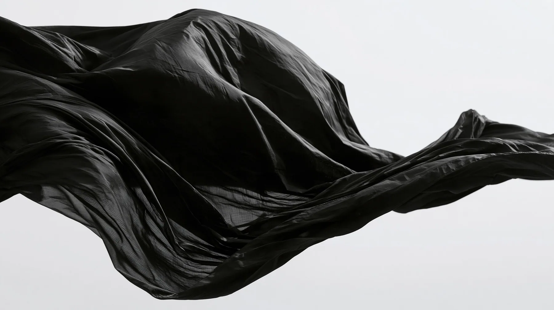 black technical nylon fabric rippling violently in wind against white, dramatic folds, high-contrast monochrome studio photograph, fine grain, no text, no letters, no logos, no watermark