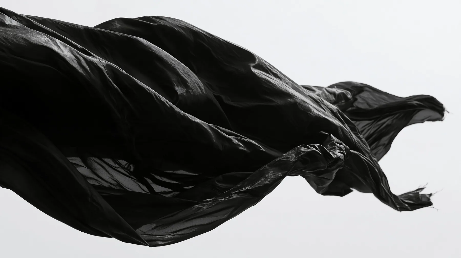 black technical nylon fabric rippling violently in wind against white, dramatic folds, high-contrast monochrome studio photograph, fine grain, no text, no letters, no logos, no watermark