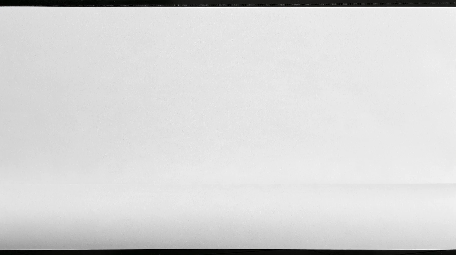 an empty sheet of grey xerox paper photographed flat, toner grain and faint scanner streaks, a hairline crop mark and a registration target near one corner, a soft fold across the lower third, a large calm field for…