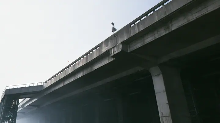 a long concrete catwalk tilting upward and lifting off into a pure white overexposed sky, the dark server hall falling away below, a small figure in a pleated skirt at the far end with the wind in her clothes,…
