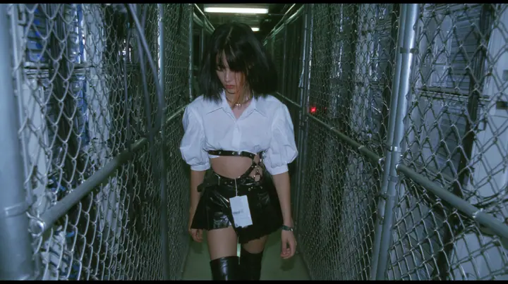 a young woman with a glossy black blunt bob with heavy bangs and one clay-orange streak, a white cropped puff-sleeve shirt, a black pleated skirt with a harness belt and a hanging white garment tag, black knee-high…