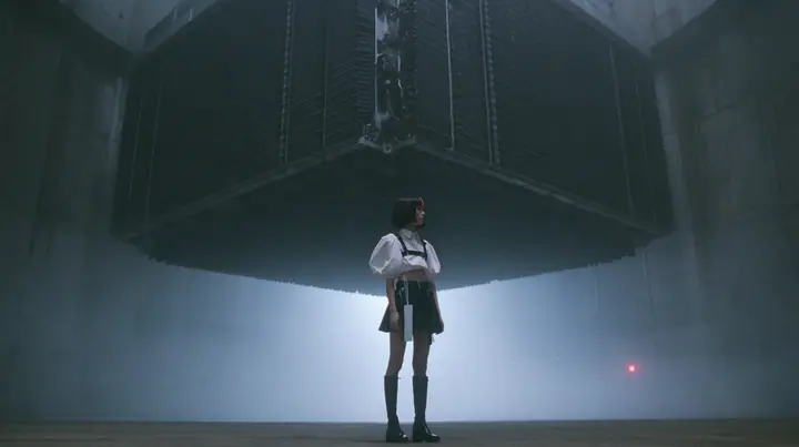 a colossal mechanical split-flap departures board hanging in a dark concrete hall, all flaps blank black, a young woman with a glossy black blunt bob with heavy bangs and one clay-orange streak, a white cropped…