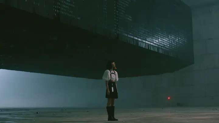 a colossal mechanical split-flap departures board hanging in a dark concrete hall, all flaps blank black, a young woman with a glossy black blunt bob with heavy bangs and one clay-orange streak, a white cropped…