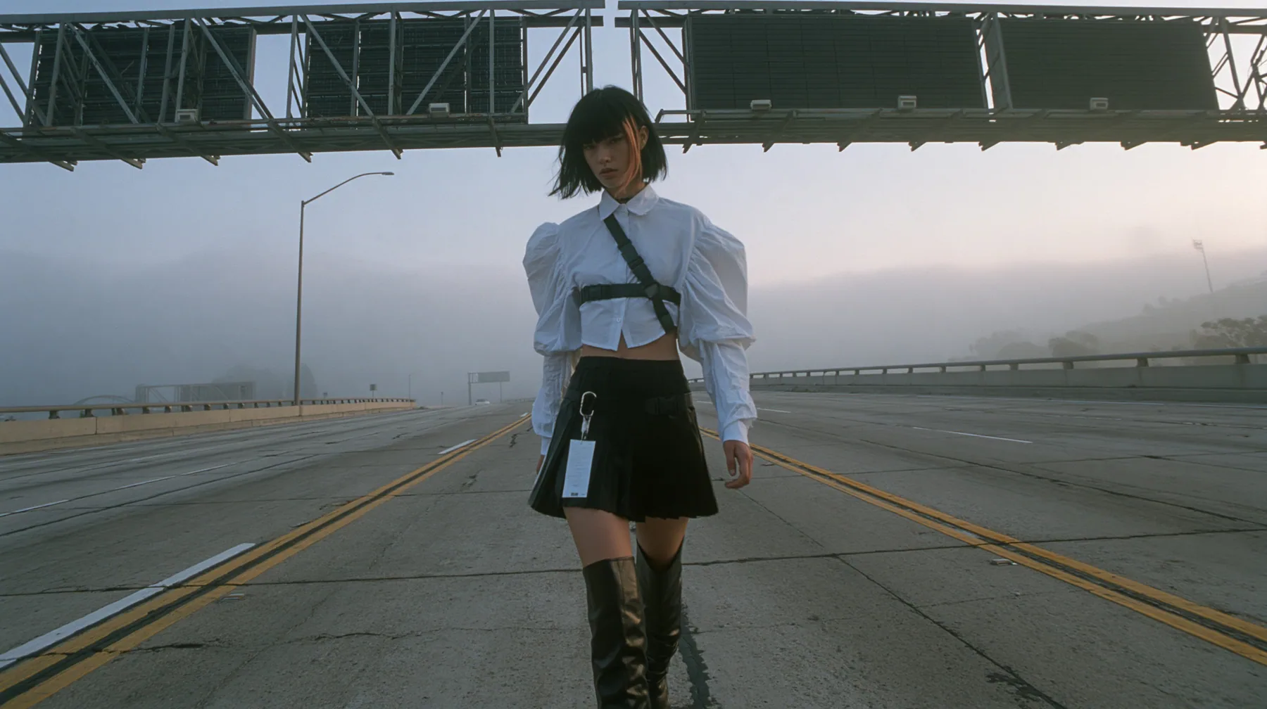 a young woman with a glossy black blunt bob with heavy bangs and one clay-orange streak, a white cropped puff-sleeve shirt, a black pleated skirt with a harness belt and a hanging white garment tag, black knee-high…