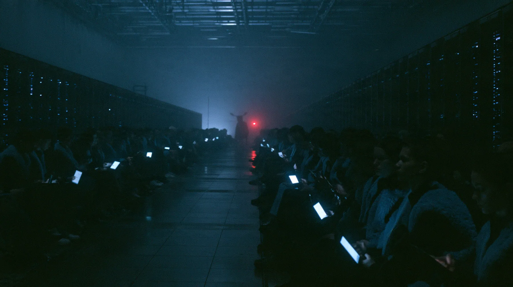 a fashion show front row inside a colossal server hall at night, rows of silhouetted guests in fleece vests holding up glowing laptops and phones, the catwalk empty and wet, fog and cold blue light, cinematic 35mm…