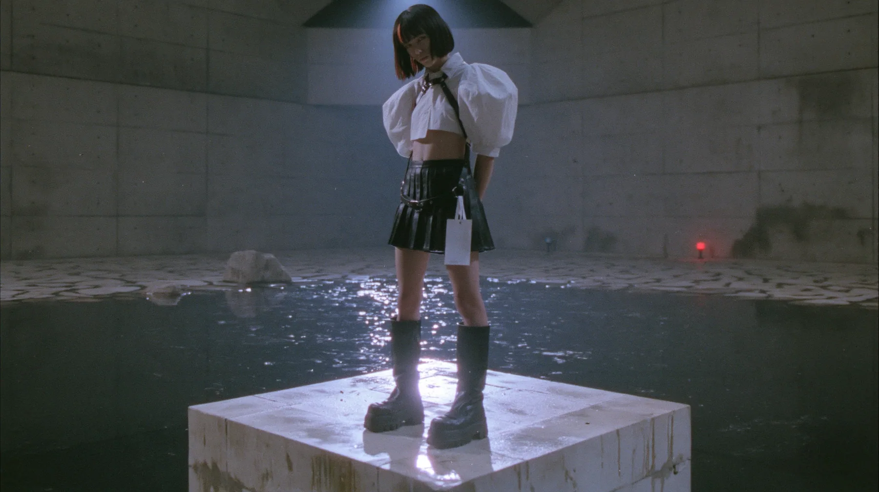 a young woman with a glossy black blunt bob with heavy bangs and one clay-orange streak, a white cropped puff-sleeve shirt, a black pleated skirt with a harness belt and a hanging white garment tag, black knee-high…