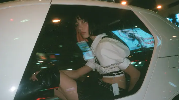 seen from outside through the rear side window of a white driverless robotaxi at night, a young woman with a glossy black blunt bob with heavy bangs and one clay-orange streak, a white cropped puff-sleeve shirt, a…