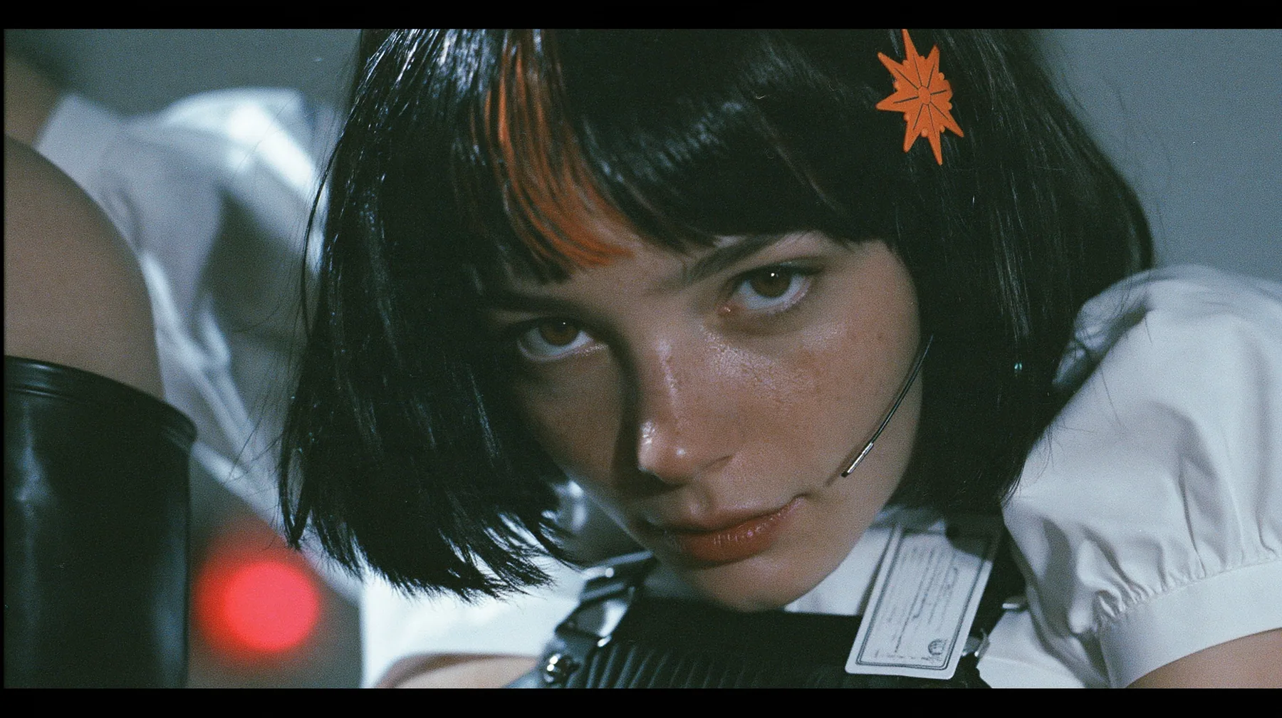 close-up portrait of a young woman with a glossy black blunt bob with heavy bangs and one clay-orange streak through the bangs, a clay-orange eight-pointed spark hair clip, a thin headset microphone, a white cropped…