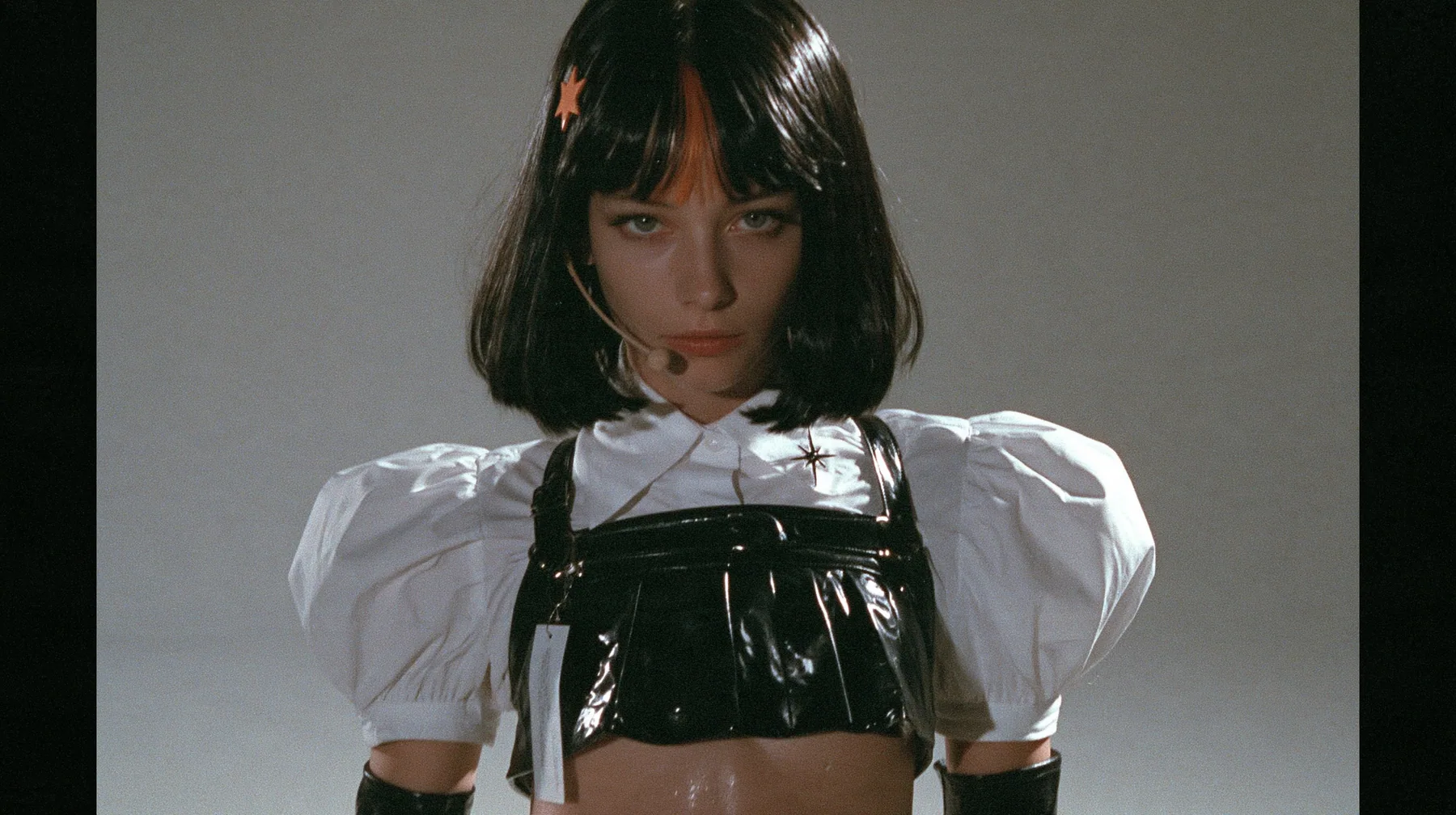 medium shot from the waist up of a young woman with a glossy black blunt jaw-length bob with heavy bangs and one clay-orange streak through the bangs, a small flat clay-orange eight-pointed star hair clip, a thin…