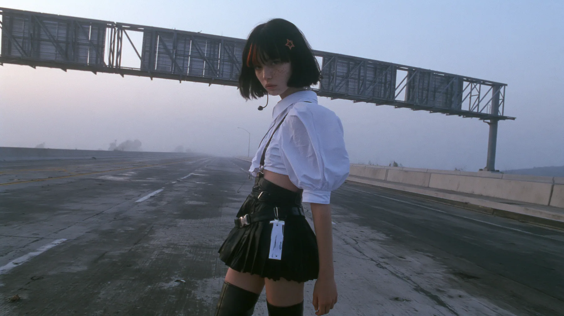 a young Caucasian American woman with pale skin and light freckles, a glossy black blunt jaw-length bob with heavy bangs and one clay-orange streak through the bangs, a small flat clay-orange eight-pointed star hair…